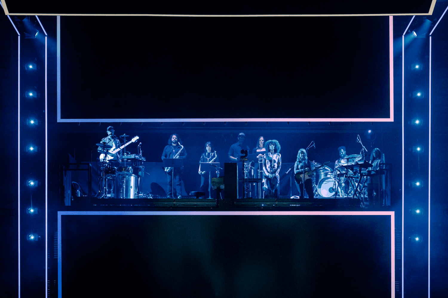 Band performing on a stage framed by blue LED panels