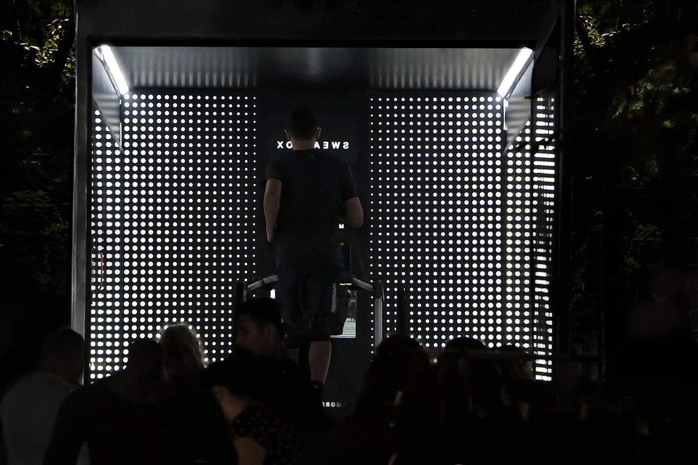 Night view of an illuminated dot-pattern screen wall with a person's silhouette inside and a crowd in the foreground