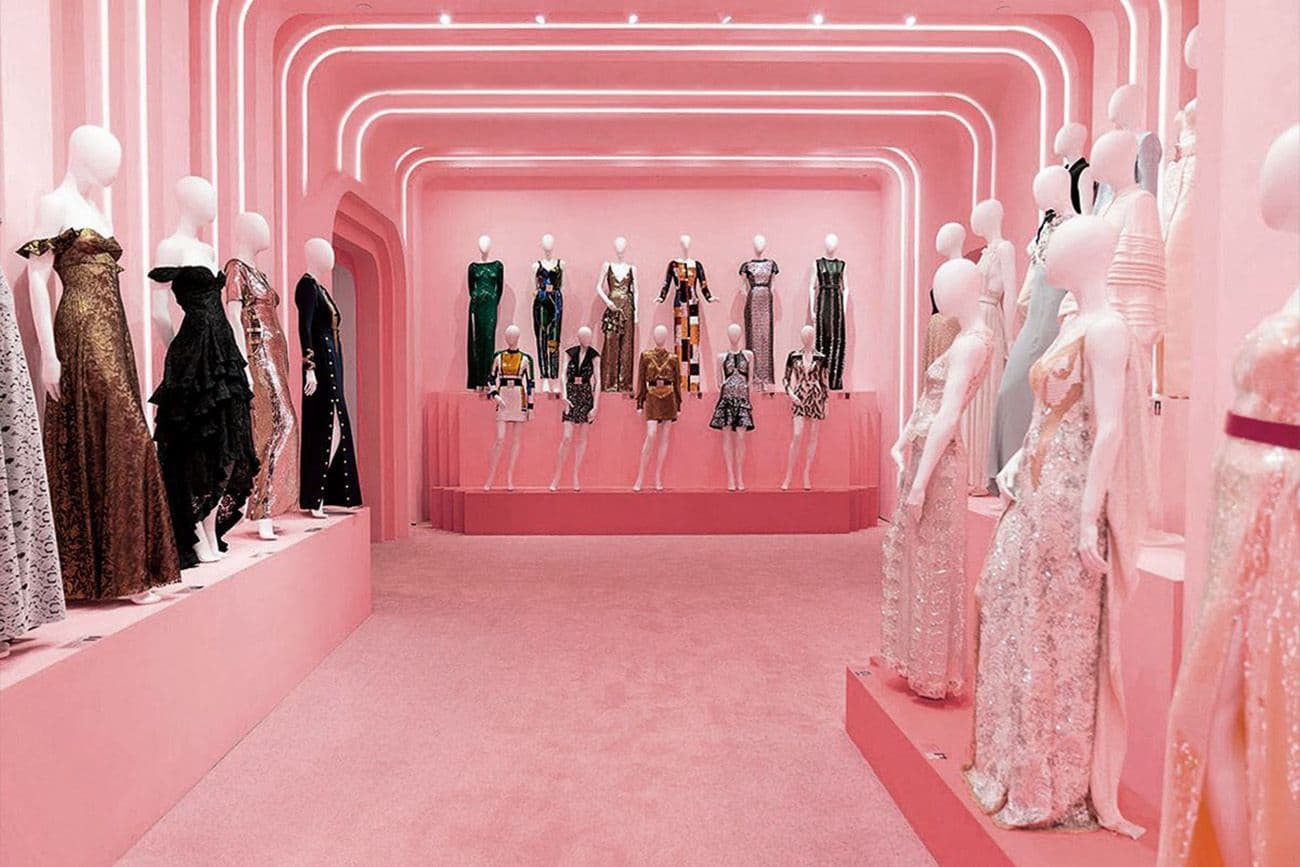 Curved pink corridor with a row of dresses displayed between mannequins.