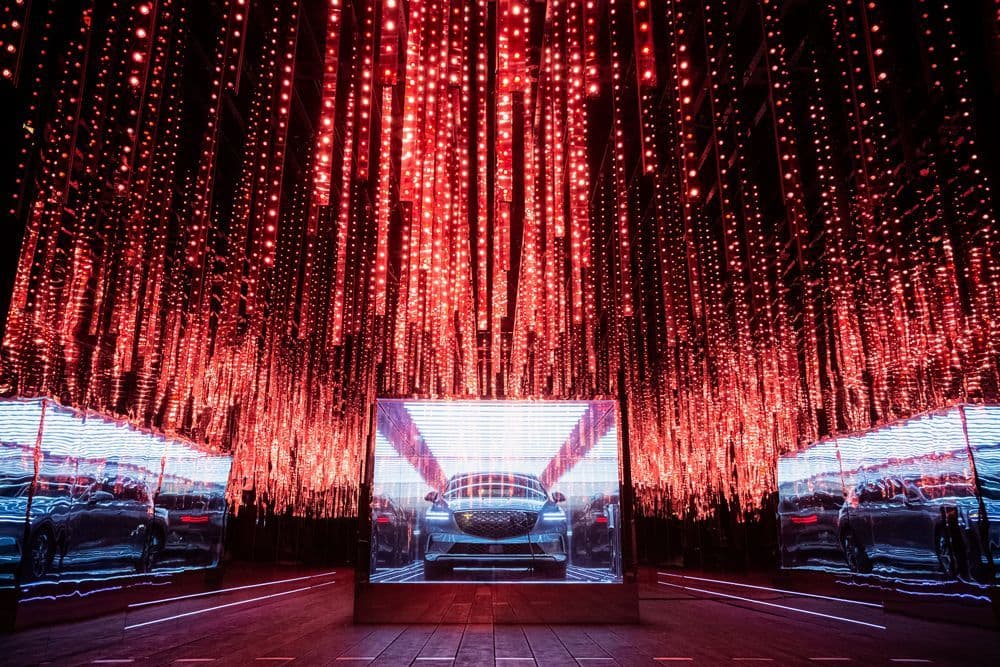 A car's rear reflected at the center of a dark tunnel lined with white neon tubes and violet string lights.
