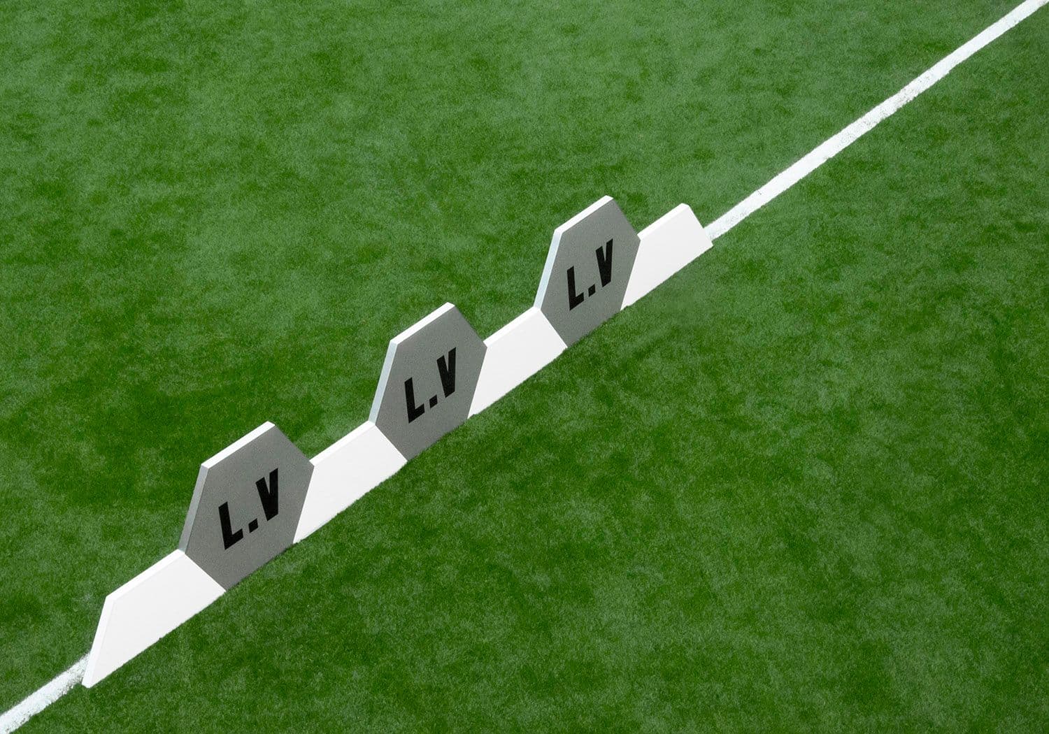 Three hexagonal LV corner flags lined up along a white sideline on the turf pitch.