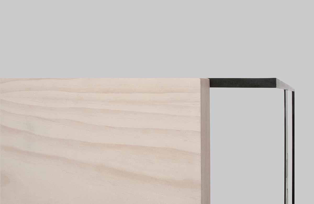 Close-up of a pale wood tabletop edge meeting a black metal frame corner.