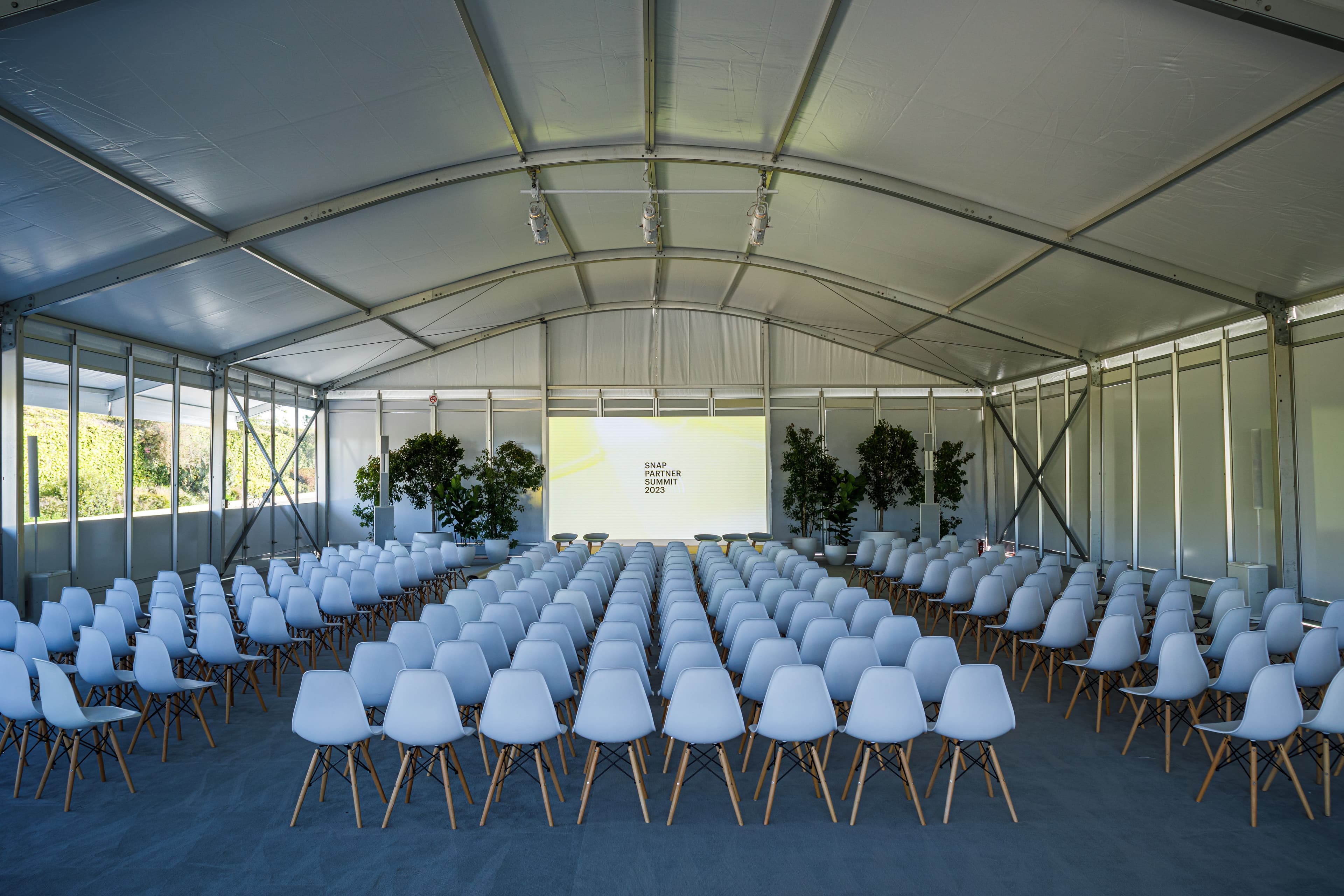 Rows of white chairs set up inside a marquee tent for a presentation.