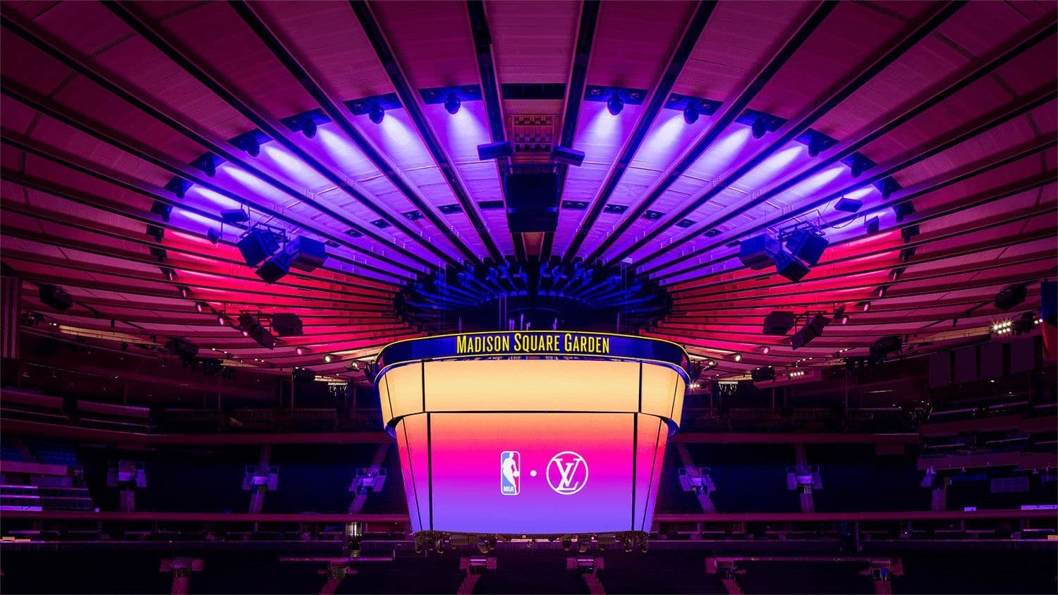 Wide interior shot of Madison Square Garden arena bowl under a radial pink and blue lighting fixture.