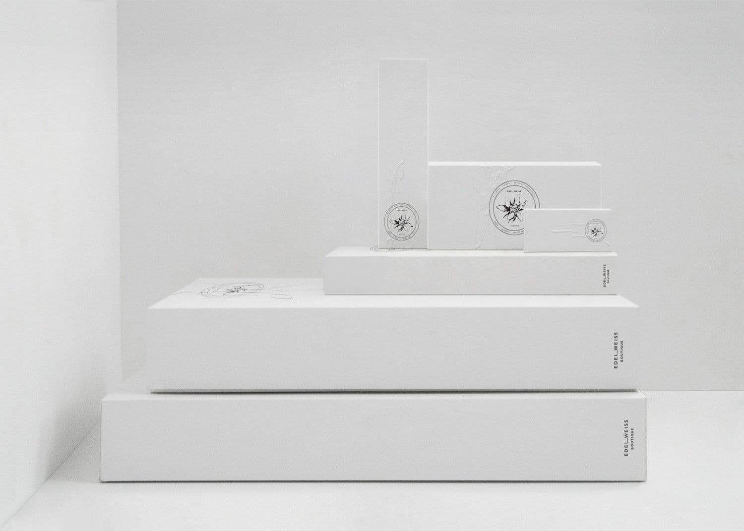 Stack of white embossed packaging boxes and cards of varying sizes, each stamped with a small circular emblem logo, against a white background.