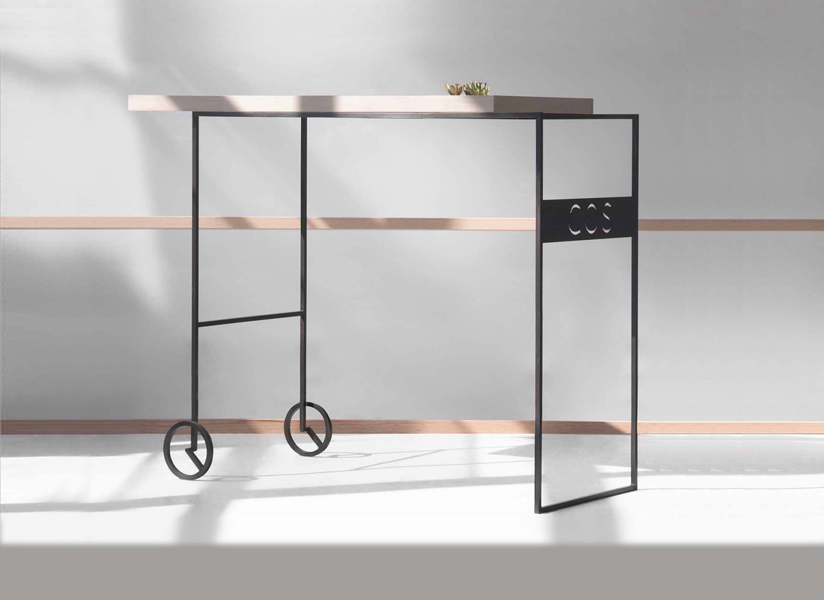 Black metal console table with wheeled feet and wood top, angled against a striped shadow on the wall.