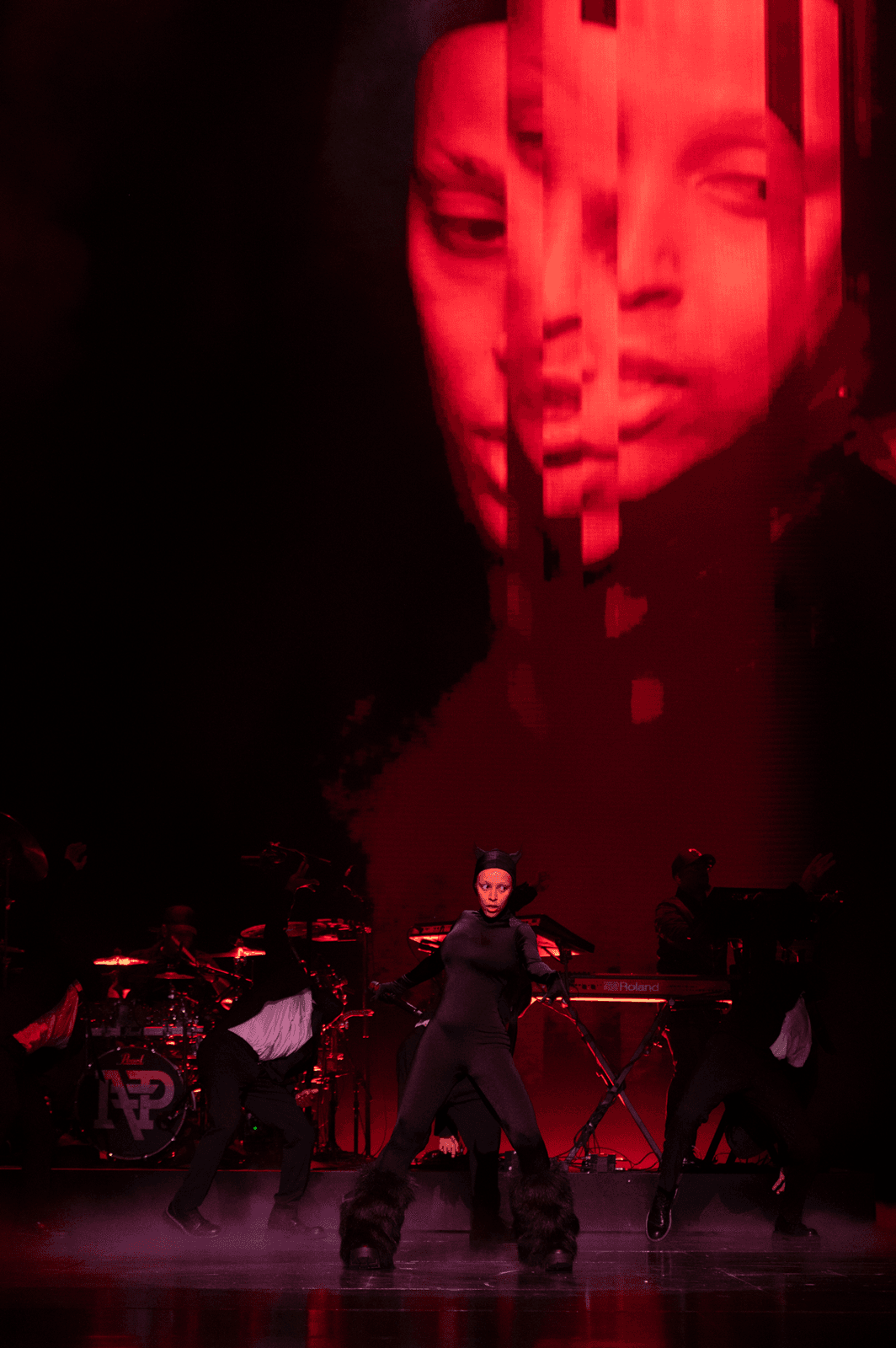 Performer singing into a microphone beside a pianist, lit in red