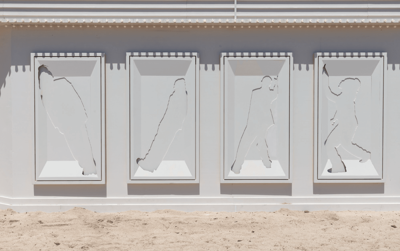A white wall with four bas-relief panels depicting golf swing silhouettes, set against a sandy beach backdrop.