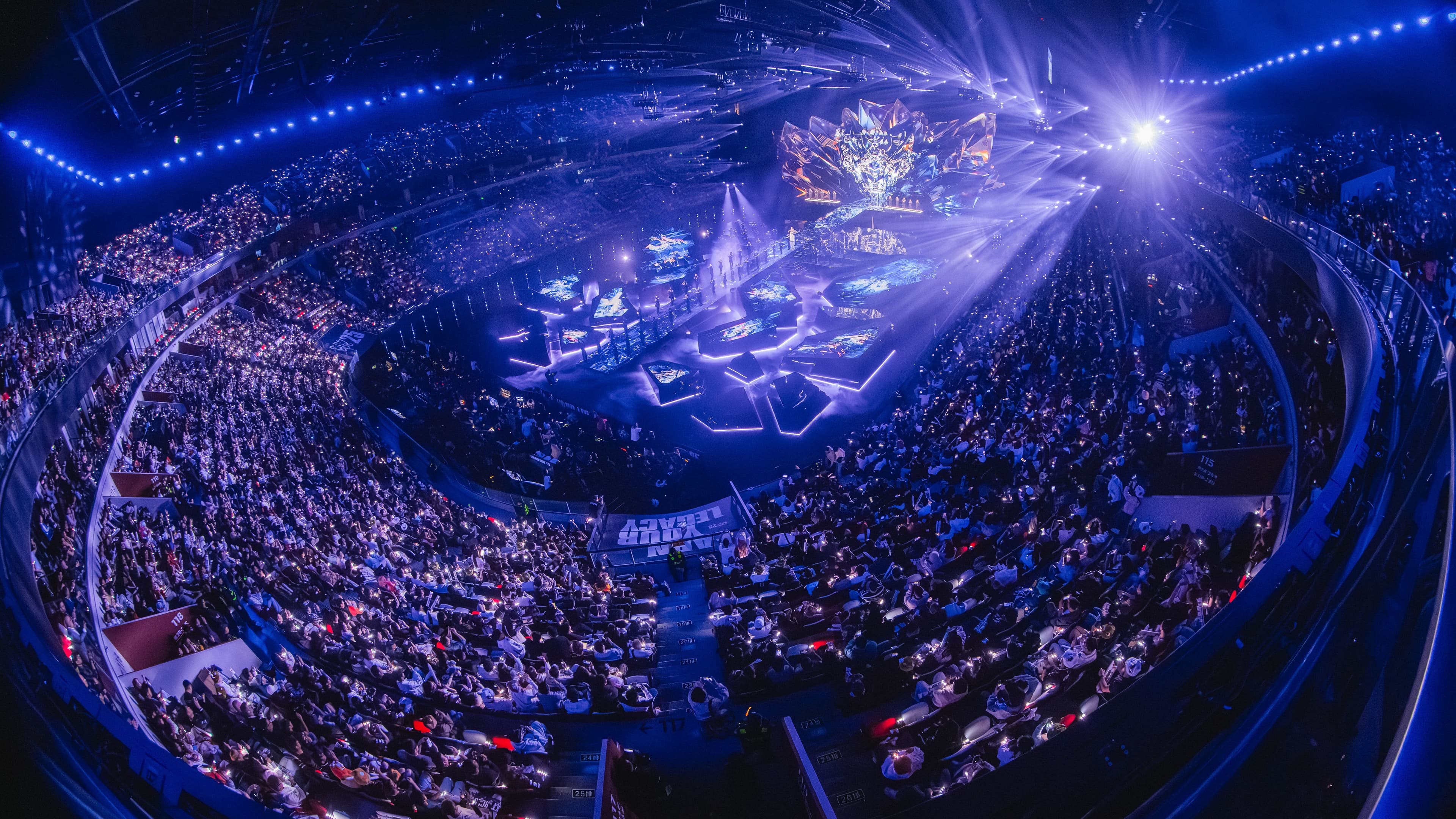 Panoramic view of a packed arena from above the stage, lit in blue.