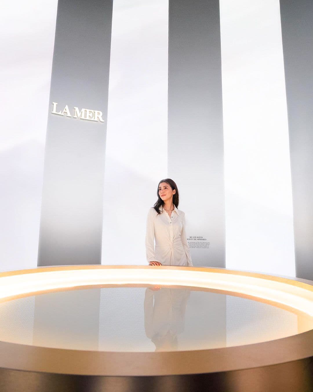 Woman standing inside a white circular backlit display beneath vertical panels bearing the La Mer logo.