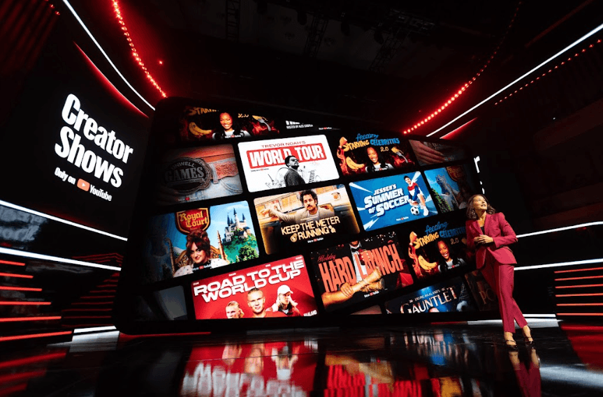 Stage screen reading "Creator Shows" displaying a grid of show thumbnails, with a host in red on stage