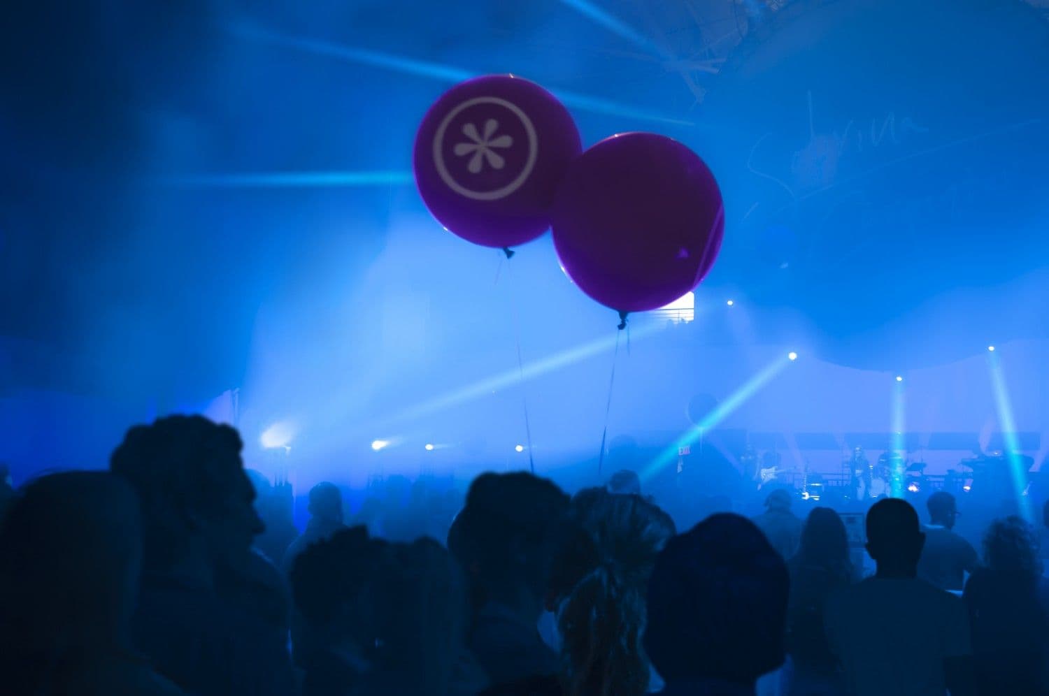 Nighttime crowd silhouetted under blue spotlights with two large illuminated balloon orbs overhead.