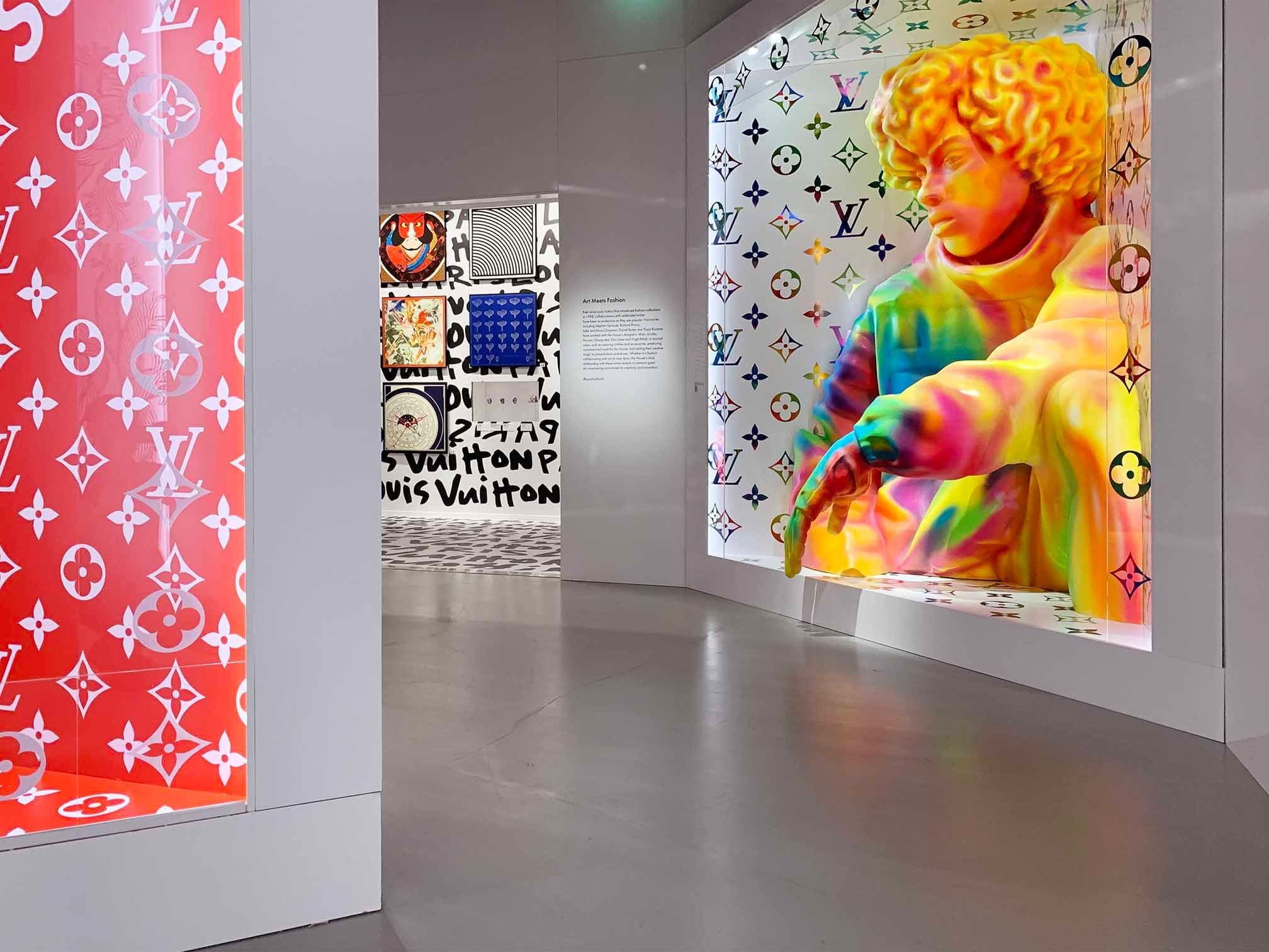 Gallery corridor with a red Louis Vuitton monogram-patterned wall leading to colorful artwork.