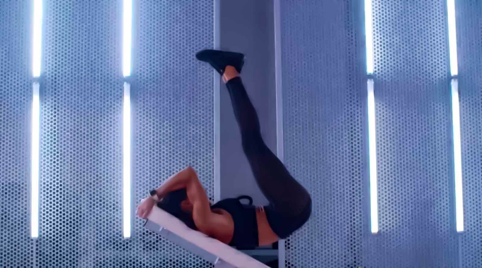 Woman performing a side plank leg raise on a bench against a wall lined with vertical LED light strips.