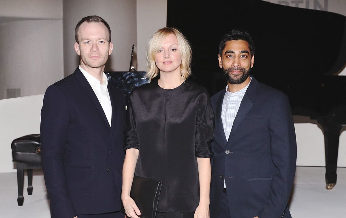 Three people posed together in front of a grand piano at an event