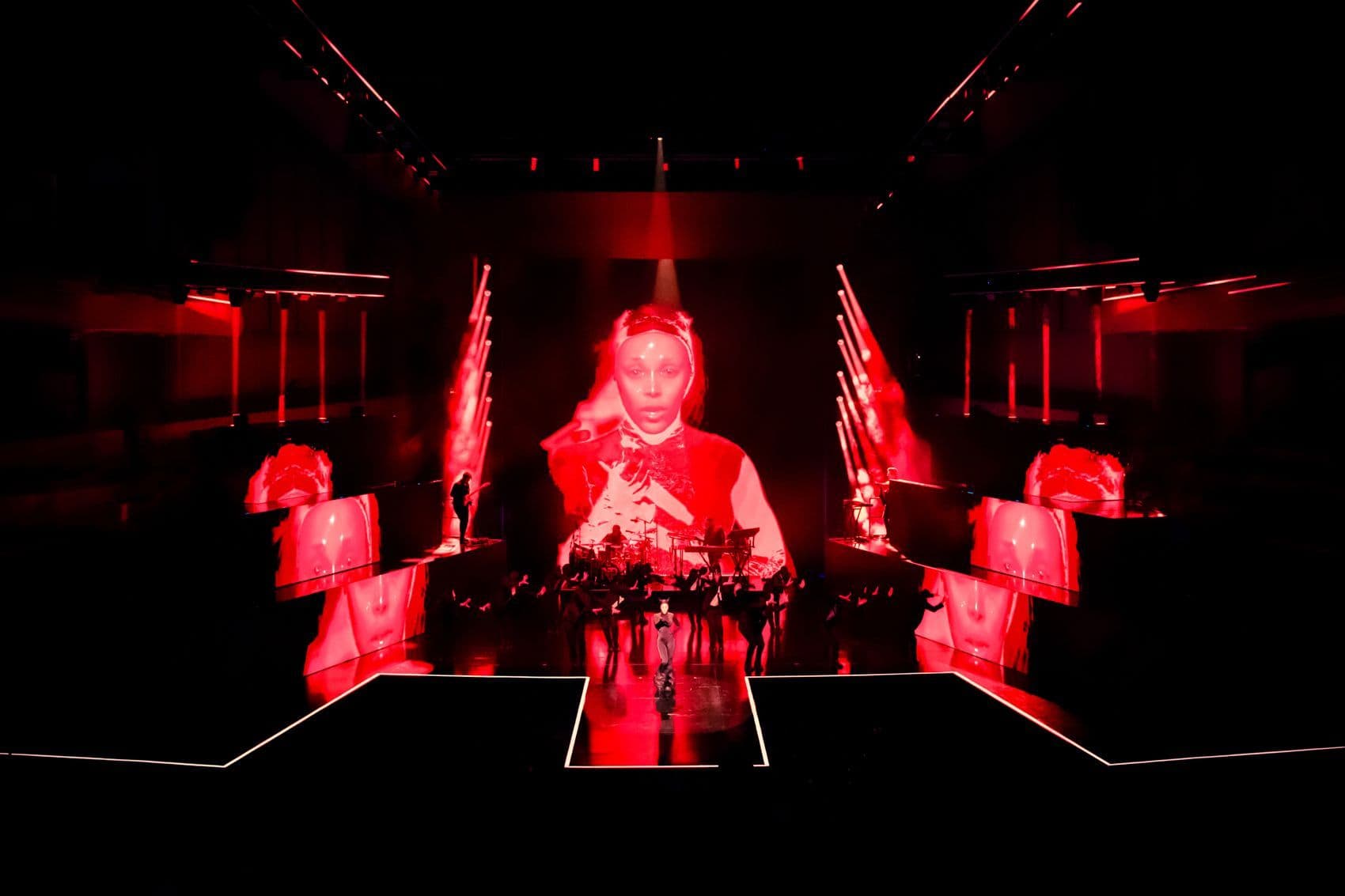 Host seated at a red-lit desk flanked by mirrored red stage panels