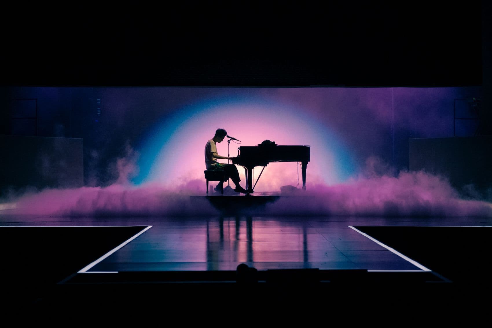 Silhouette of a performer at a grand piano lit by a blue glowing arch