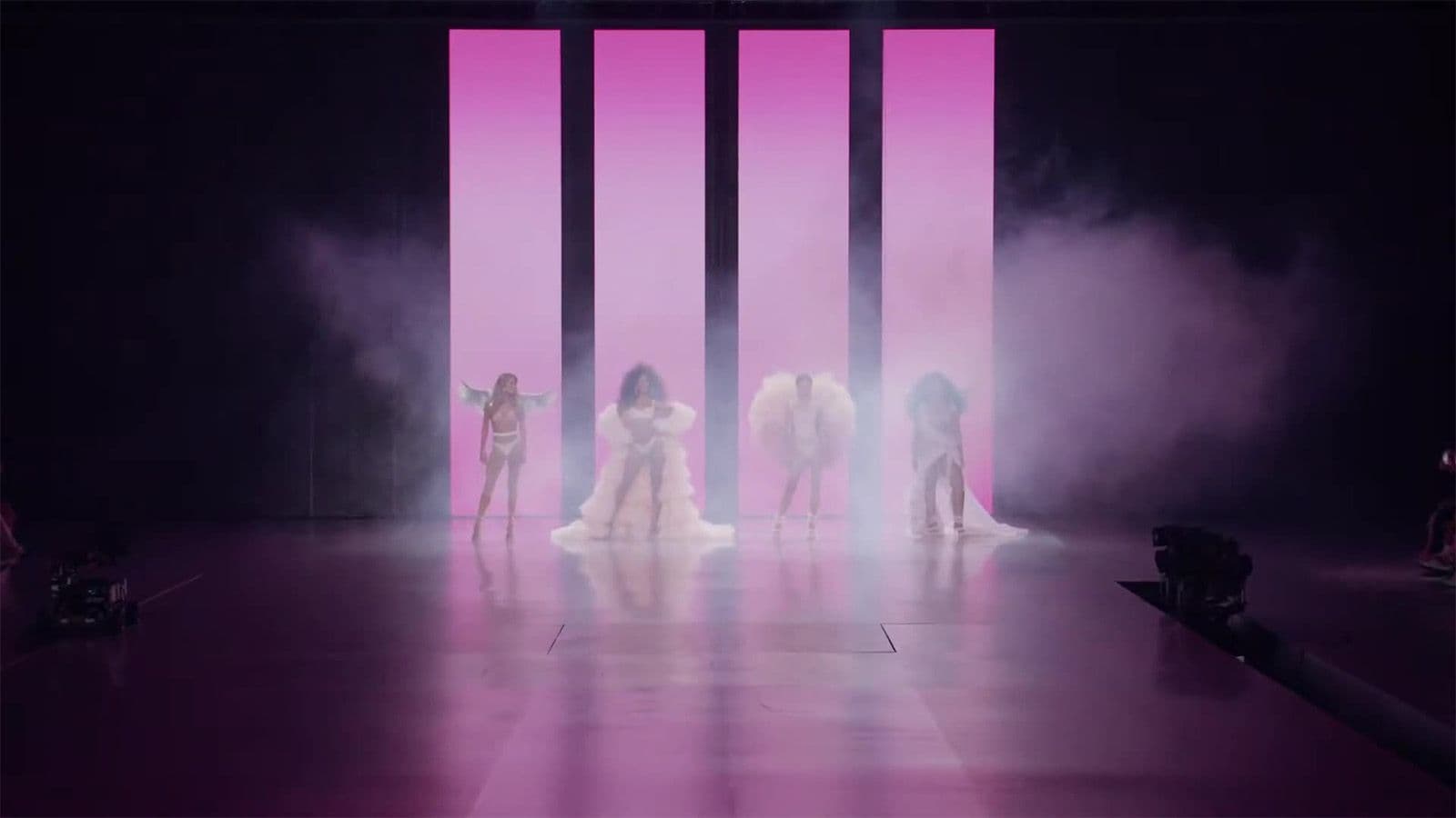 Models in pink gowns walk the runway through heavy fog, lit by vertical magenta light bars.