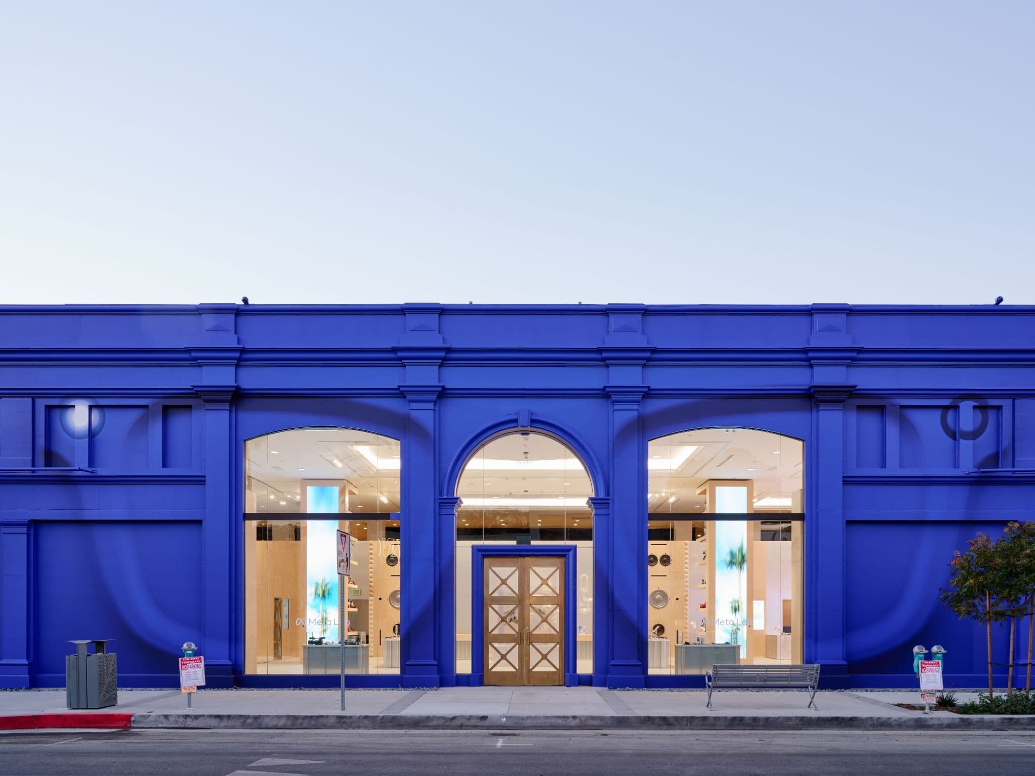 Storefront of a cobalt-blue building with arched display windows and a wood-paneled entrance door, viewed head-on.