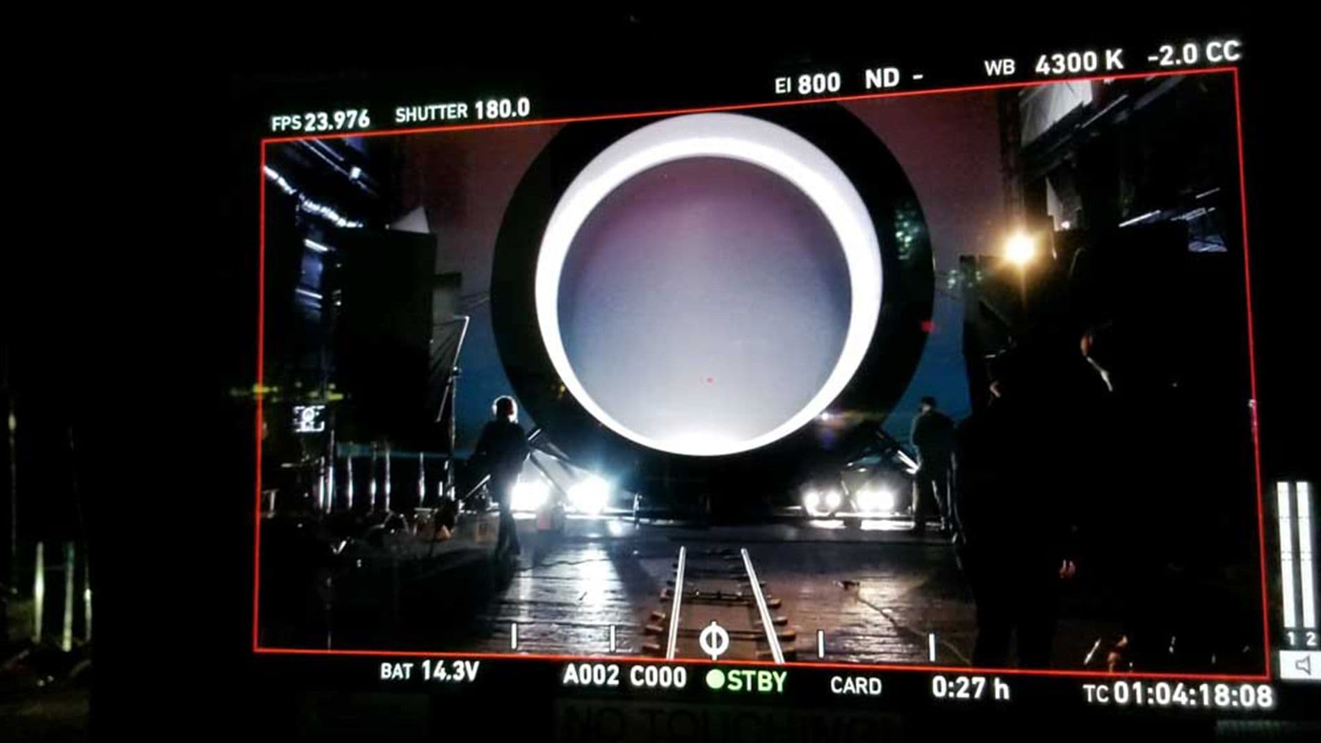 Camera monitor on set showing a glowing white ring lit from behind, with lens and recording data overlaid on the display.
