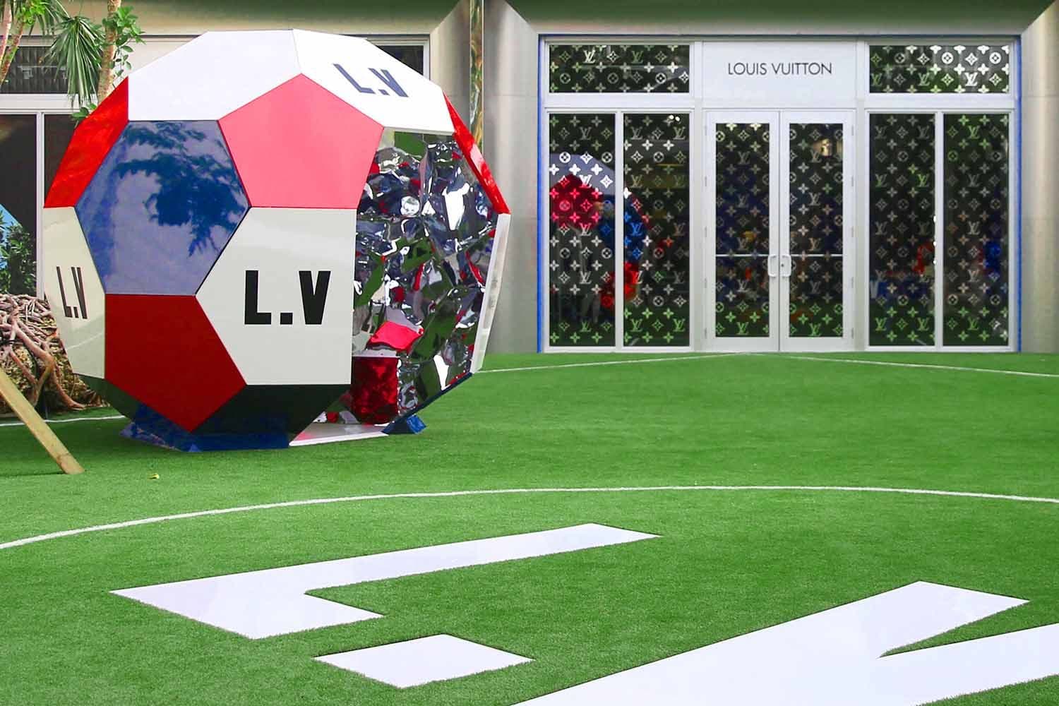 Giant Louis Vuitton monogram soccer ball display beside the storefront entrance, with a number seven marking on the turf.