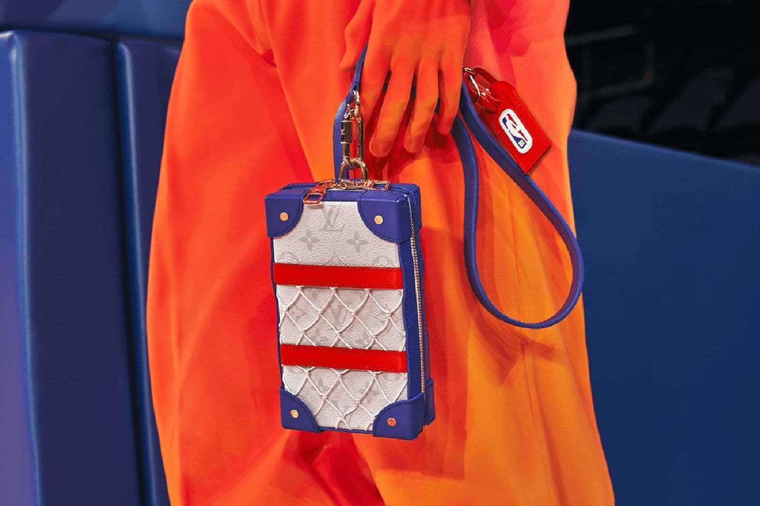Model in an orange tracksuit holding a blue and white quilted crossbody bag.