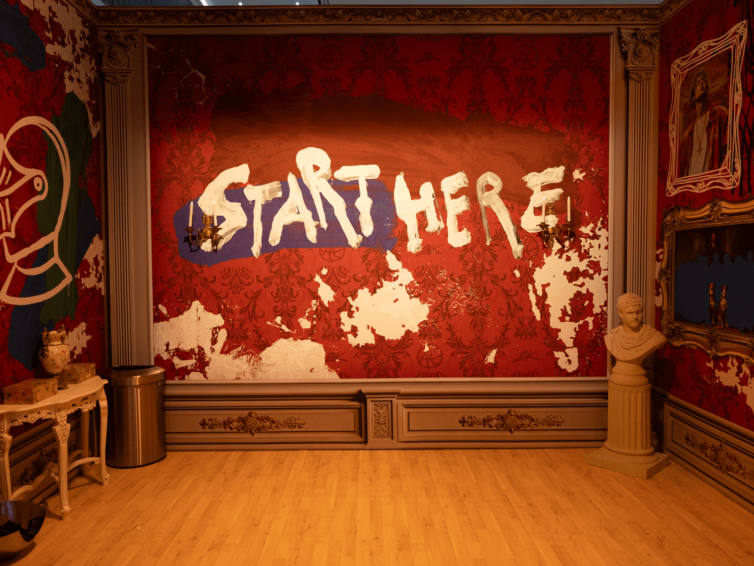 A visitor looks up at two large illuminated portrait frames hung on a red patterned wall inside the gallery installation.