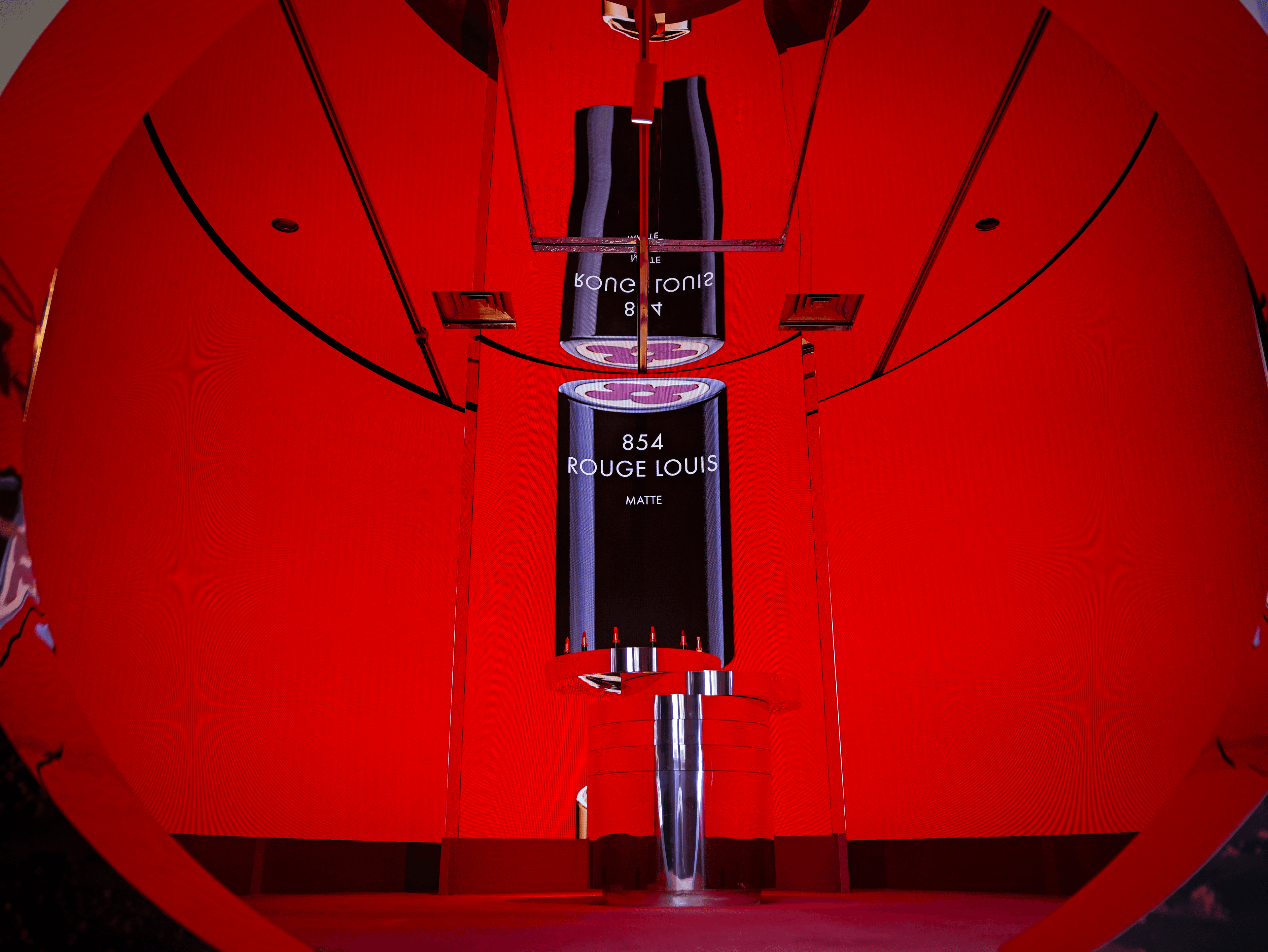 Close-up of vertically hung illuminated product panels reading '854 Rouge Louis' inside a red circular tunnel display.