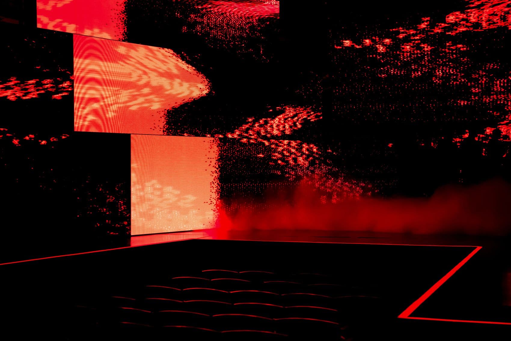 Wide shot of a blue-lit arena stage with a band performing above a seated audience.