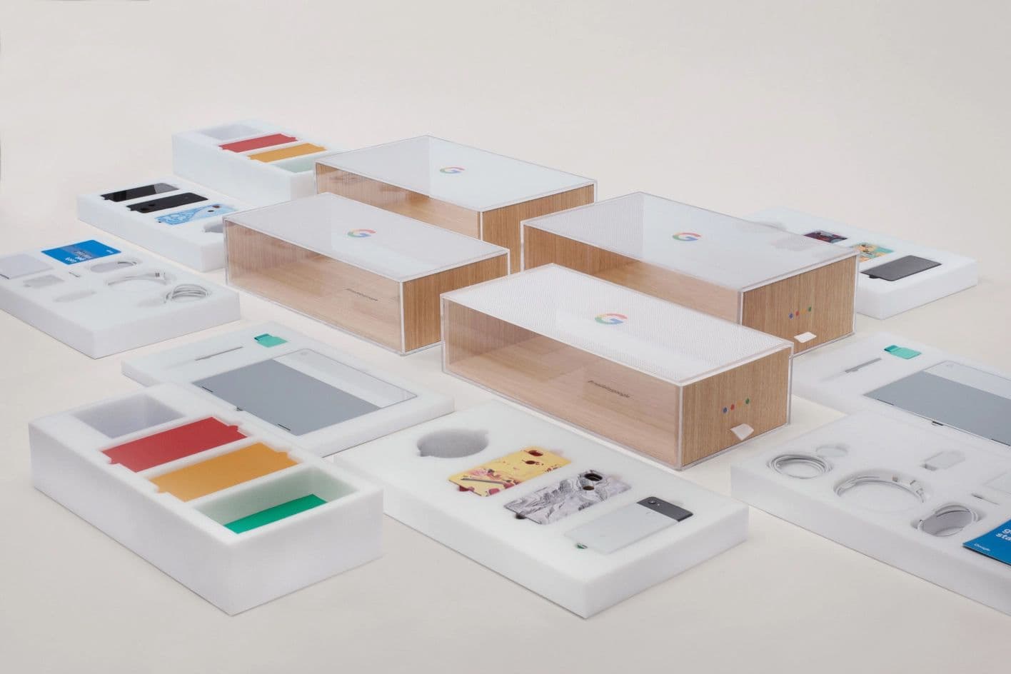 Assortment of Google device packaging in wood and frosted acrylic, alongside colorful foam accessory trays and product inserts.