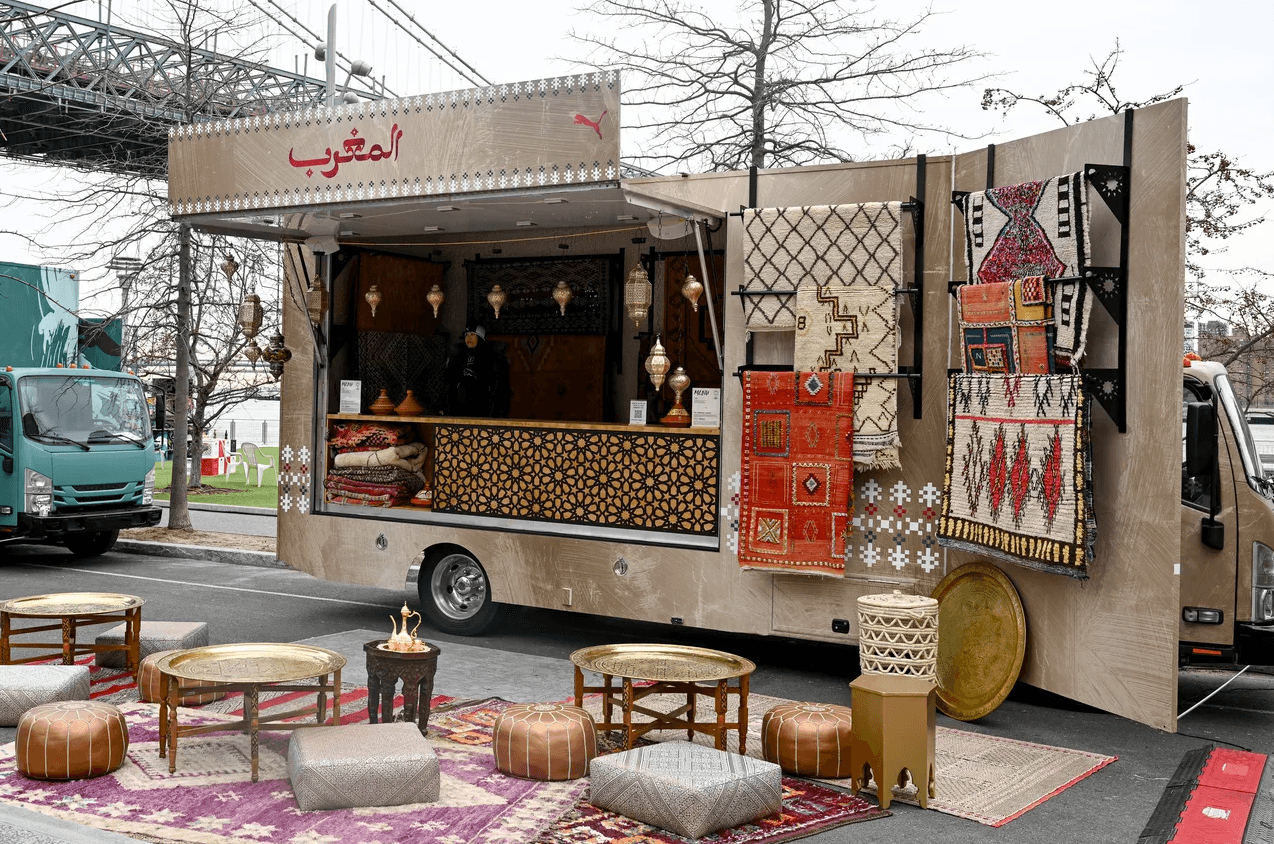 Moroccan-themed shipping-container kiosk with patterned rugs, low seating, and lanterns set up as a lounge area.