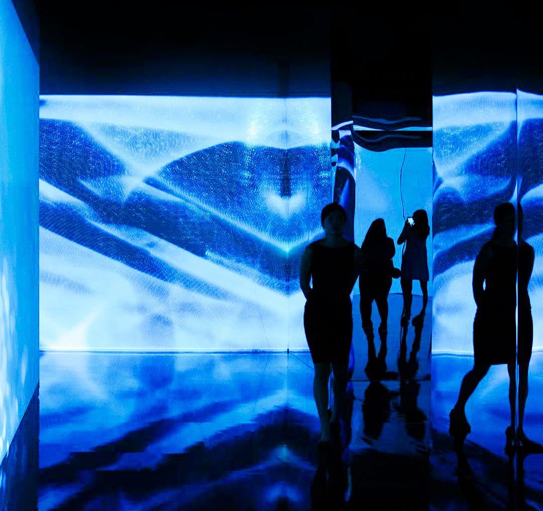Wide view of a blue-lit room with wave-pattern walls and visitors' silhouettes walking through.