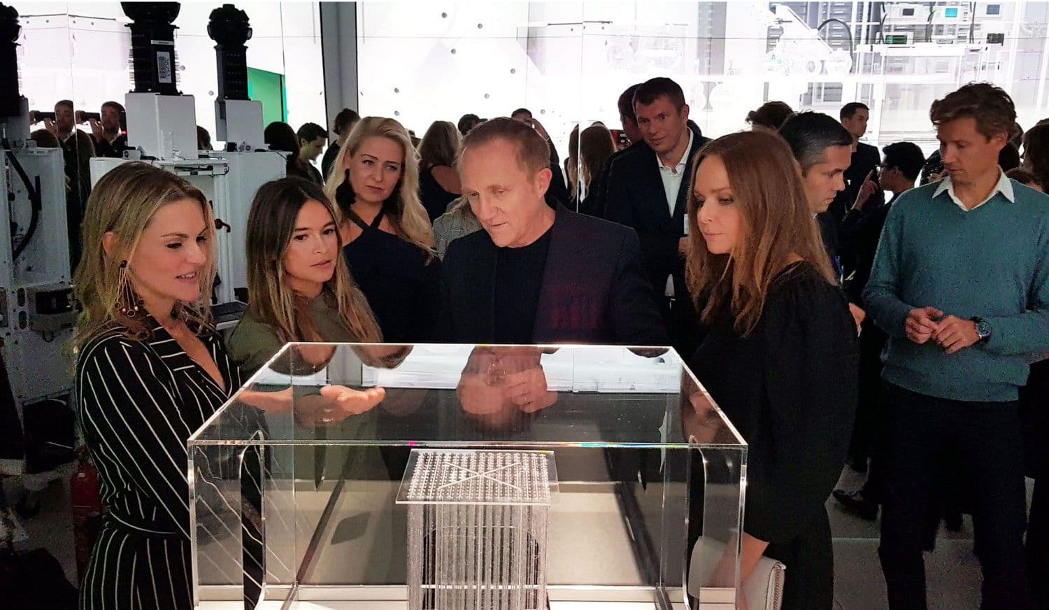Group of attendees examining a fabric sample in a glass display case at an event.