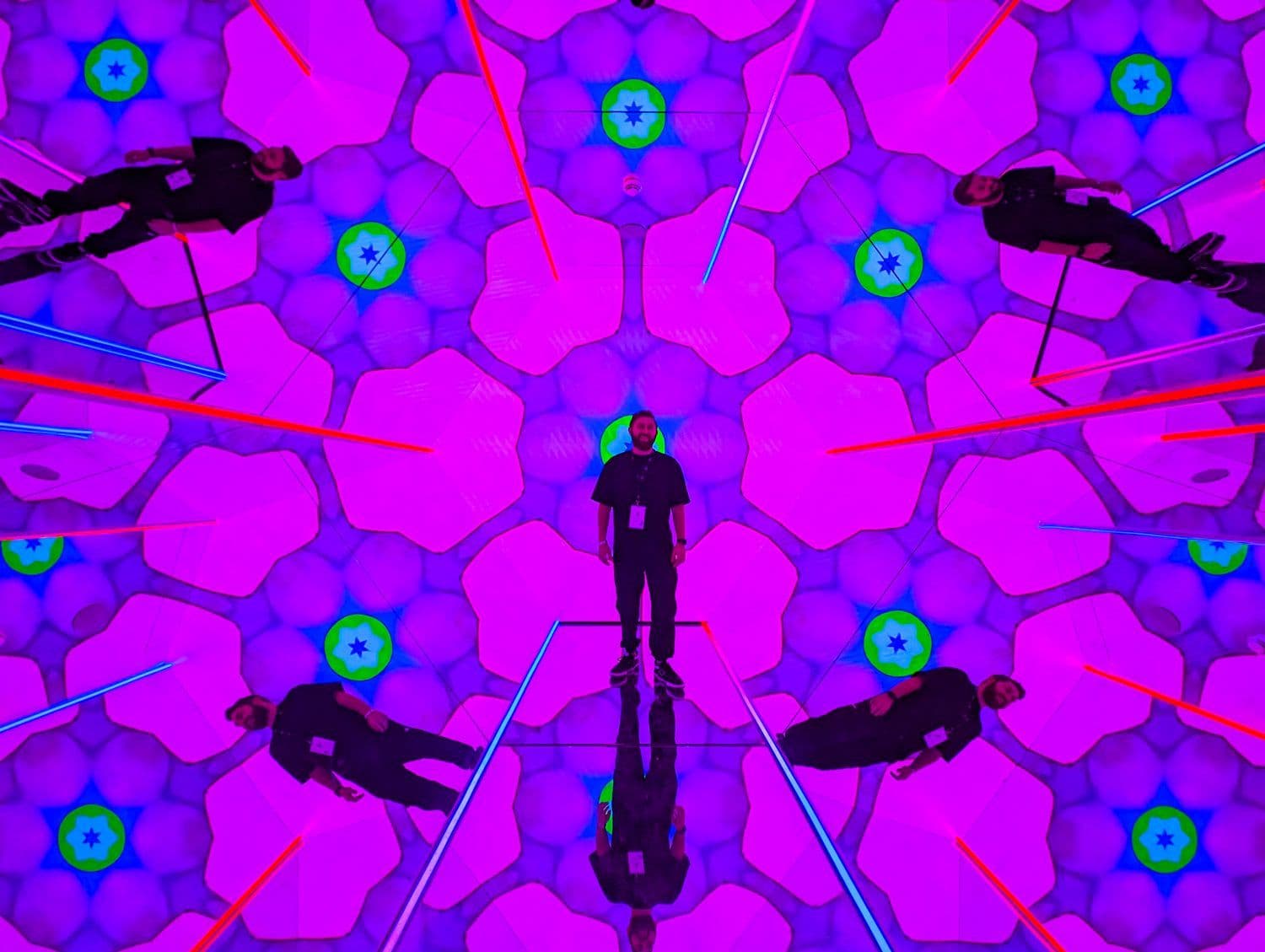 A kaleidoscopic purple digital tunnel with silhouetted figures and red laser beams, centered on a person walking down a lit runway.
