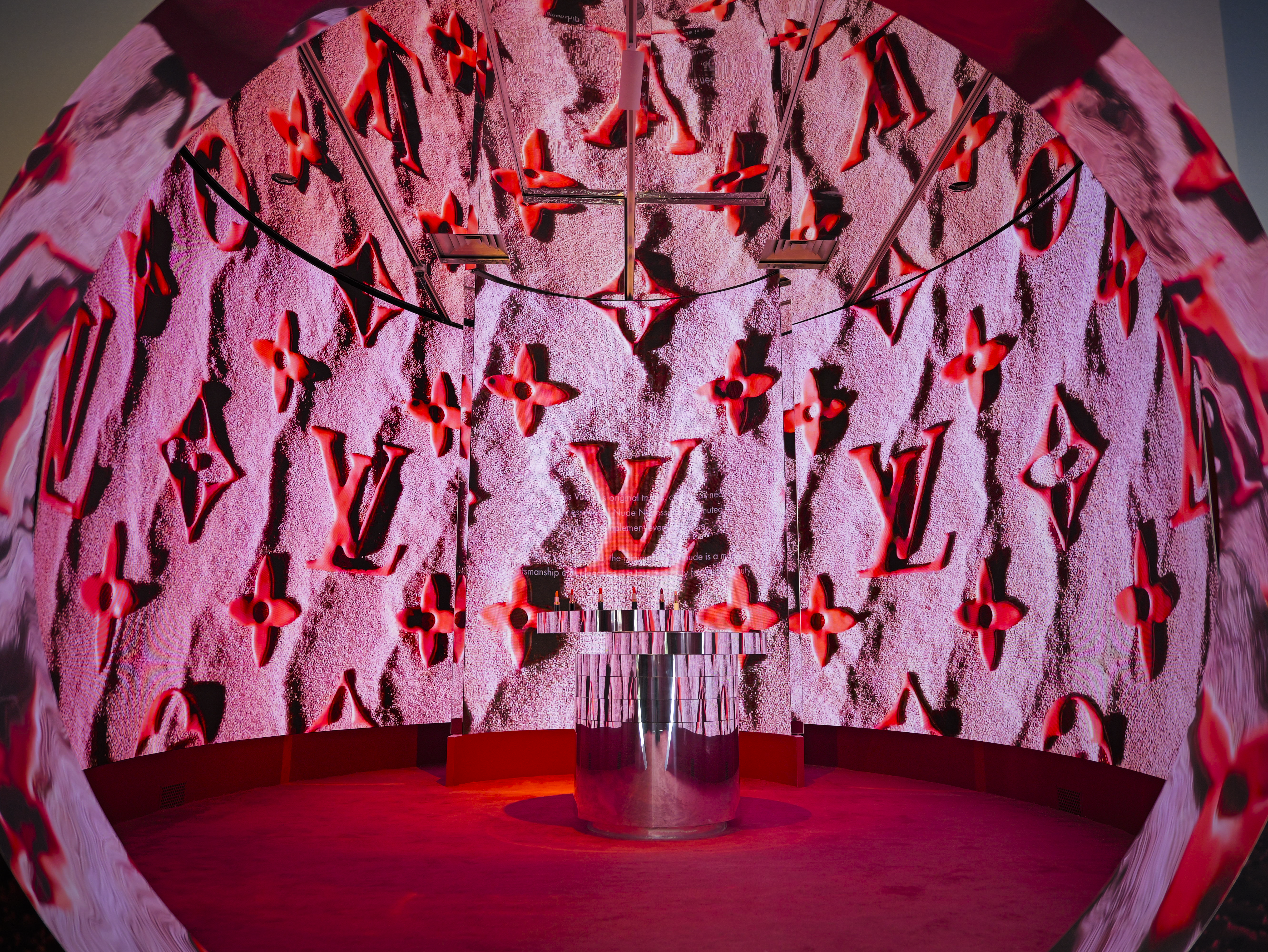 Pink circular tunnel room with the Louis Vuitton monogram pattern on textured walls, cylindrical plinth at center.