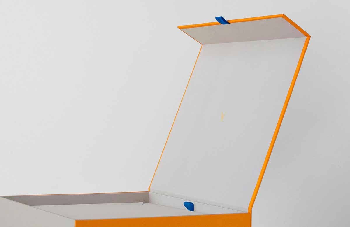 Side view of an open orange box with a white interior lining and a blue tab pull on the lid's edge.