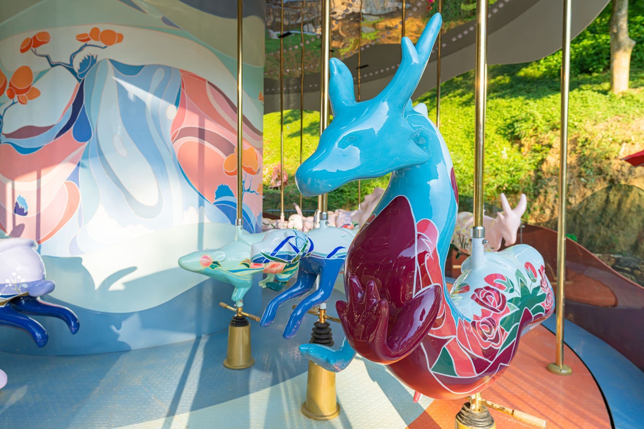 Carousel horse figure painted in pastel abstract patterns, suspended among other animal figures under a canopy.