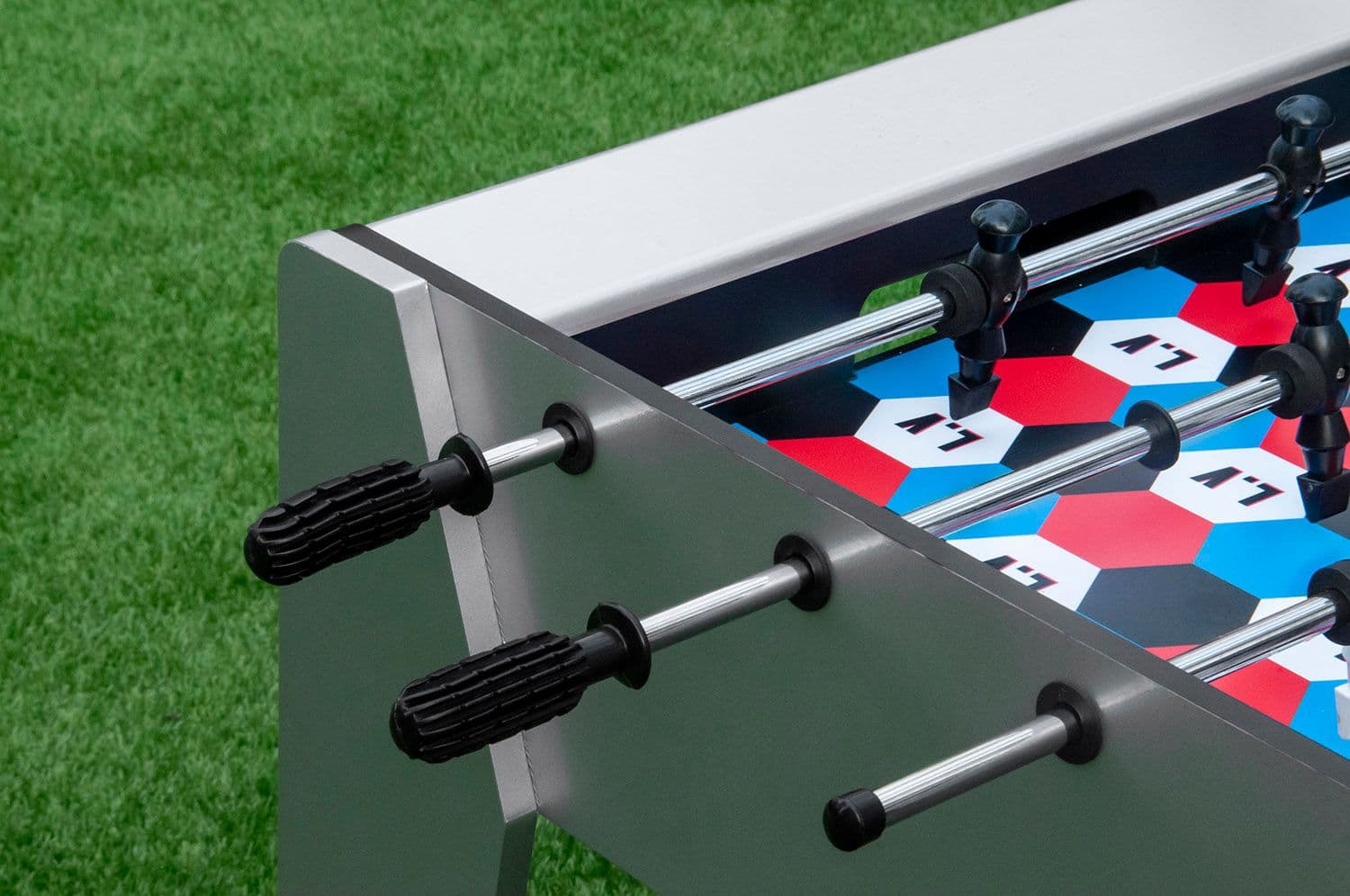 Close-up of a foosball table with monogram-patterned player figures on artificial turf.