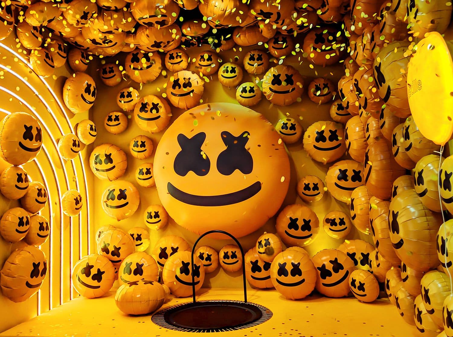 Archway installation covered in glowing orange emoji face sculptures with a marshmello mask centerpiece.