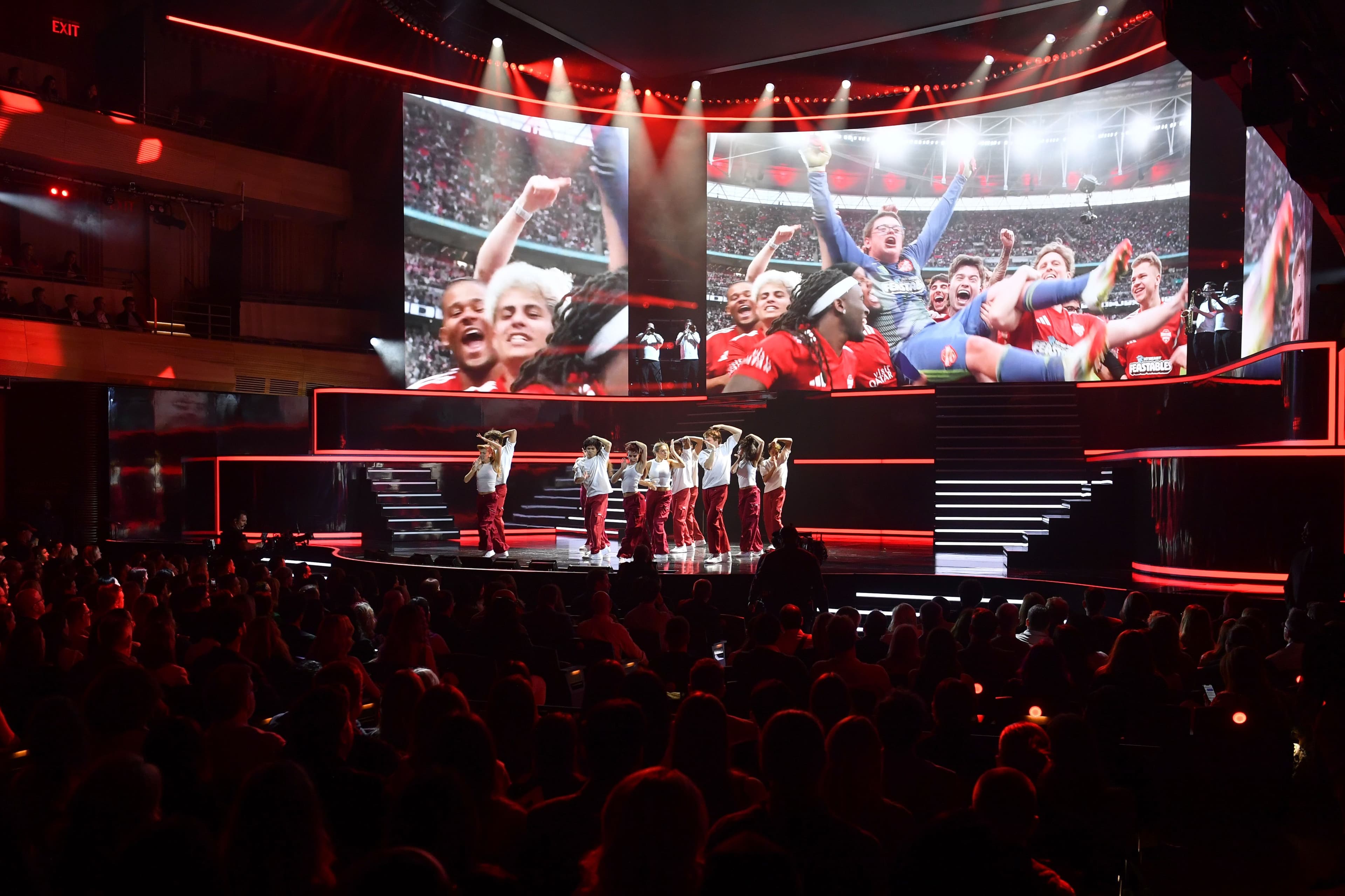 Wide shot of the audience cheering with arms raised toward the stage screens