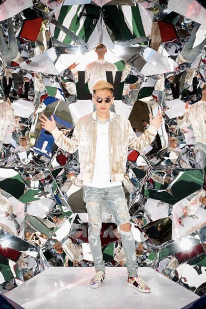 Man in a bomber jacket and sunglasses posing inside a mirrored kaleidoscope photo installation.