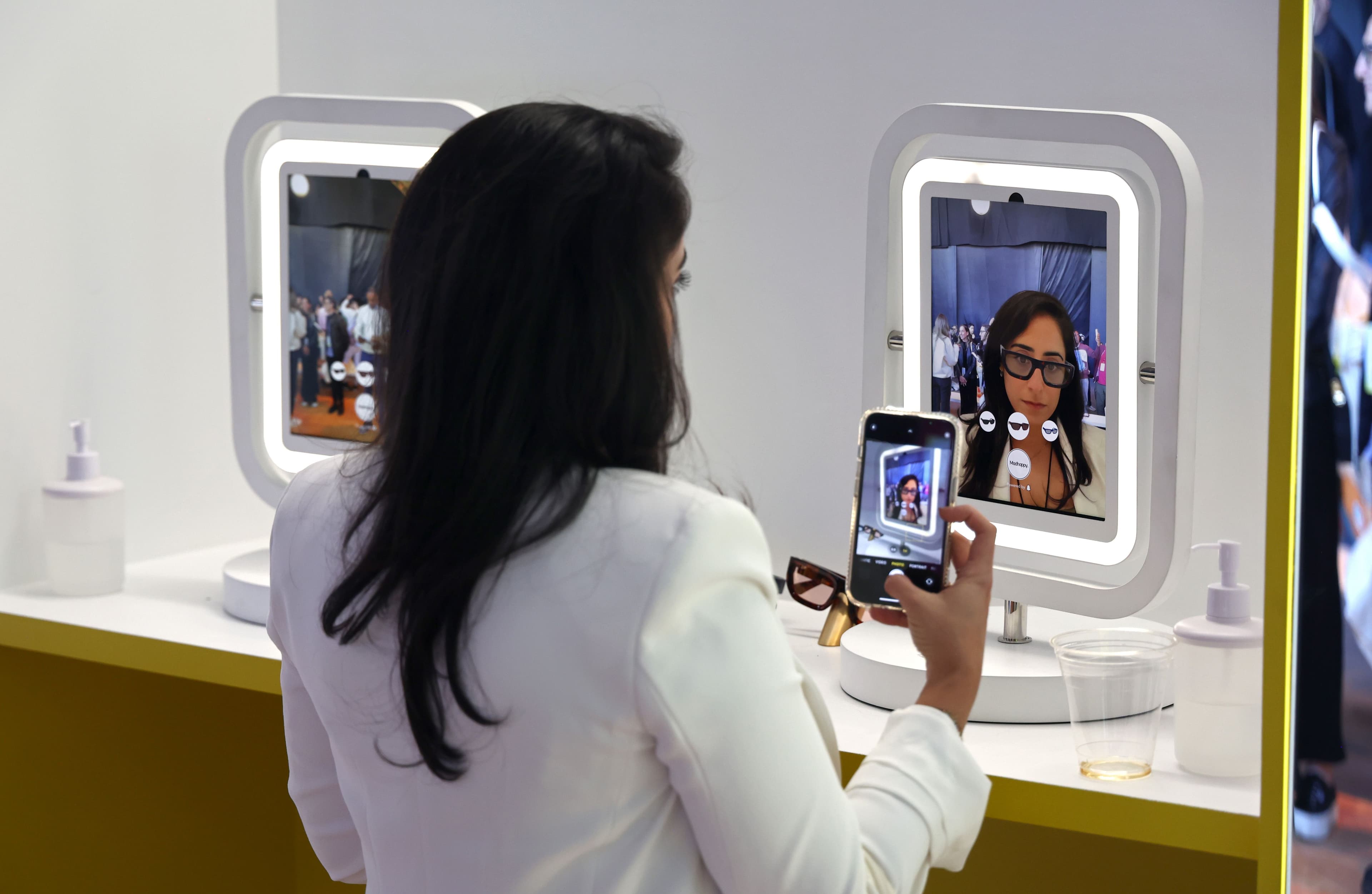 Woman photographing herself in a lit vanity mirror display.