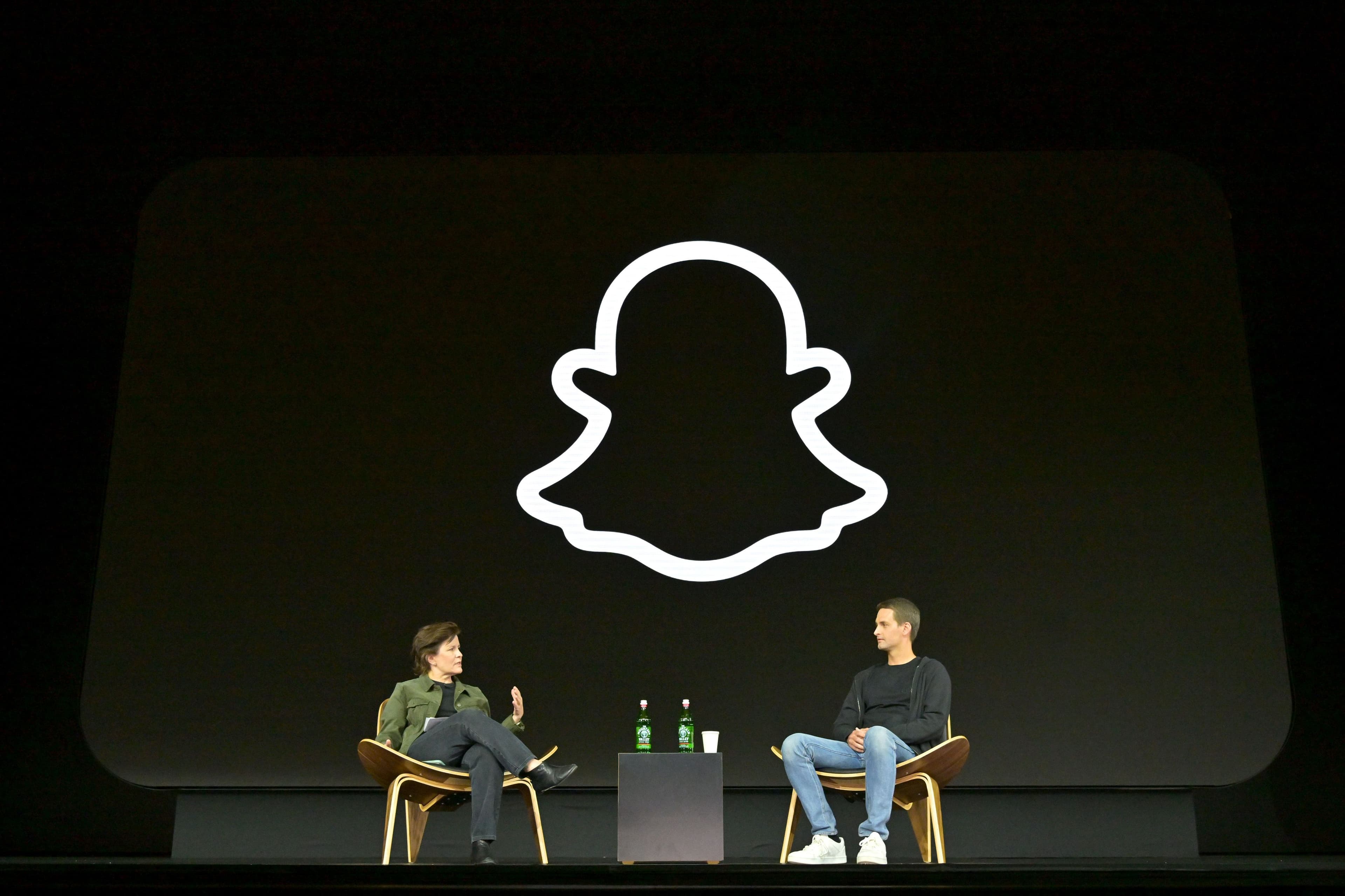 Snapchat ghost logo on a large screen above two people seated for an on-stage conversation.
