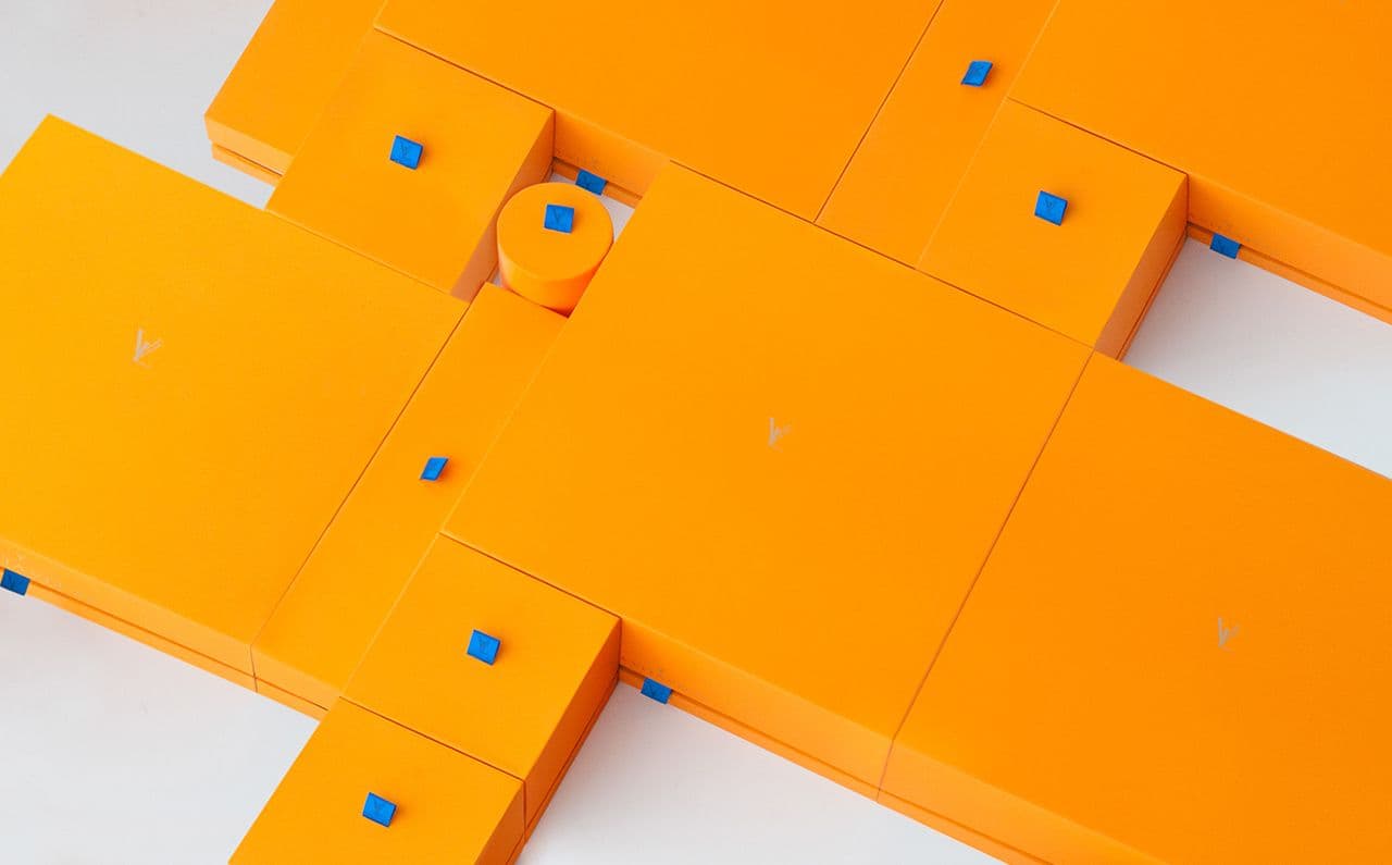 Overhead close-up of interlocking orange box lids with small blue corner tabs and faint embossed logo marks.