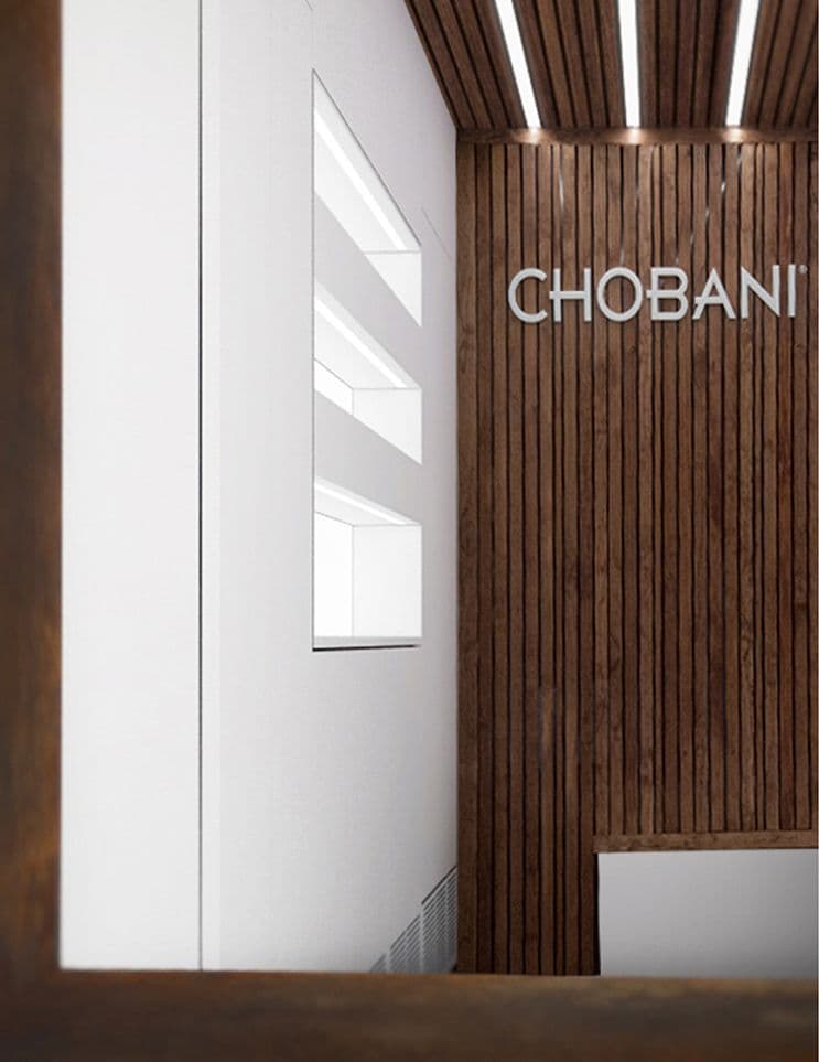 Interior corner with wood-slat paneling, the CHOBANI wordmark, and a window lit by ceiling strip lighting.