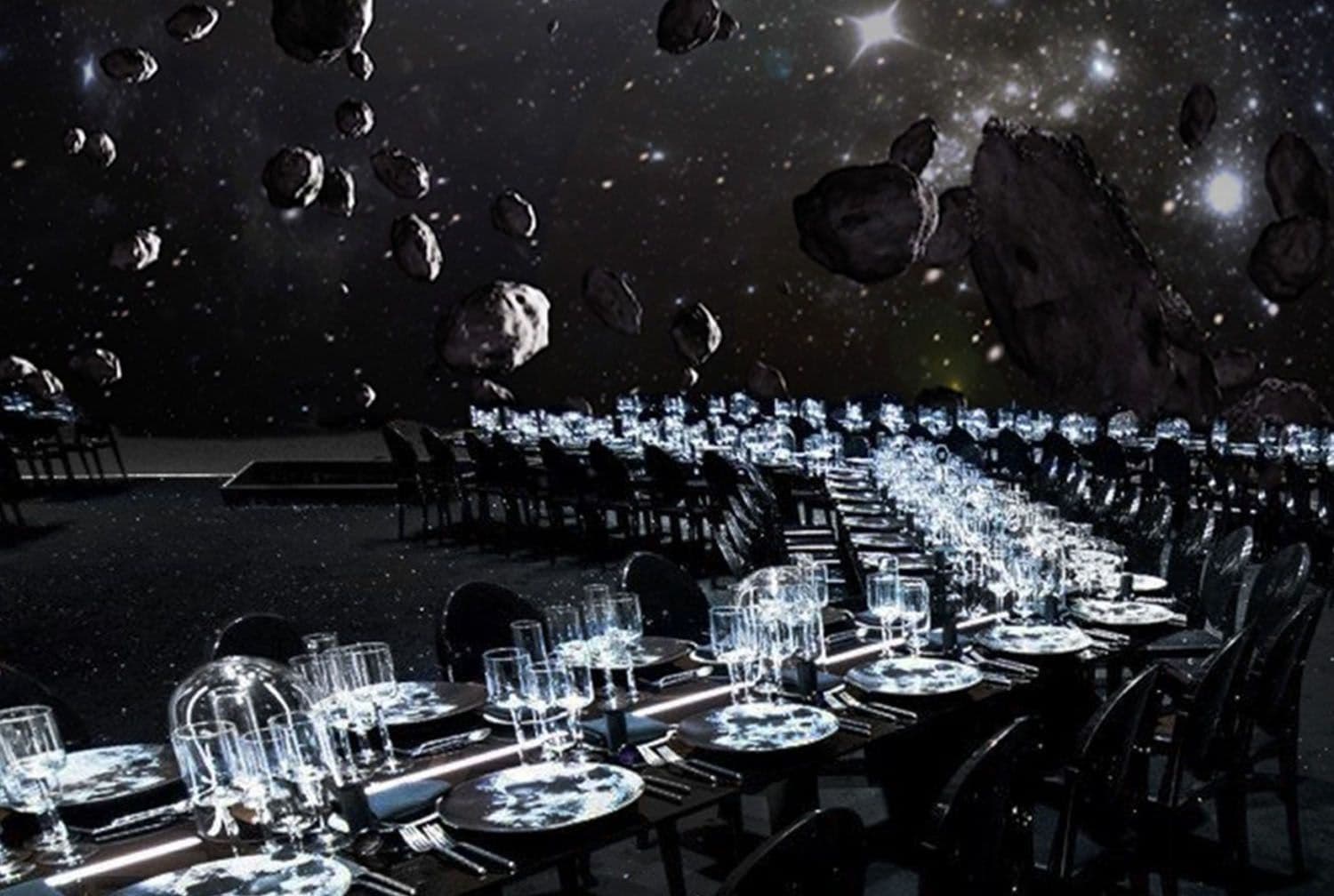 Long banquet tables set with glassware and place settings beneath a ceiling projection of asteroids and stars.