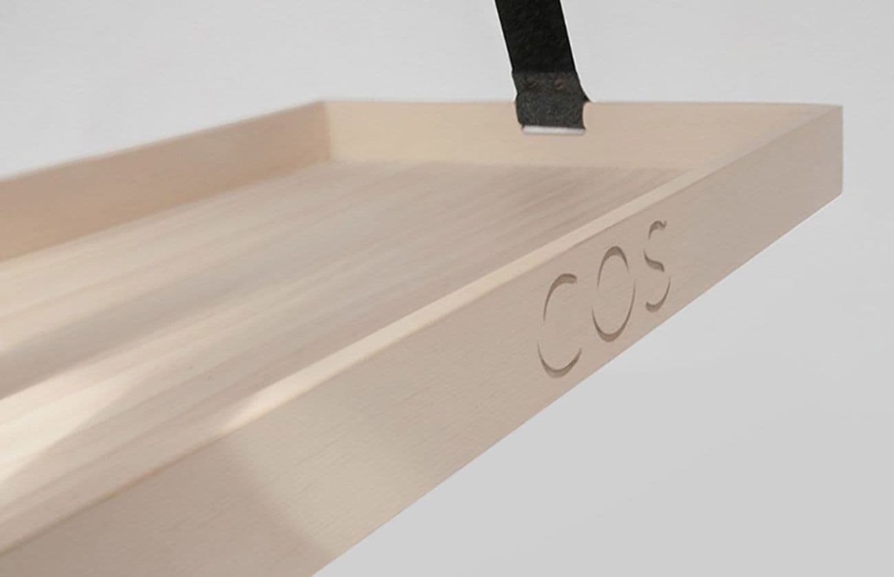 Close-up of a pale wood tray corner with a black felt strap, a black blade resting on the surface.