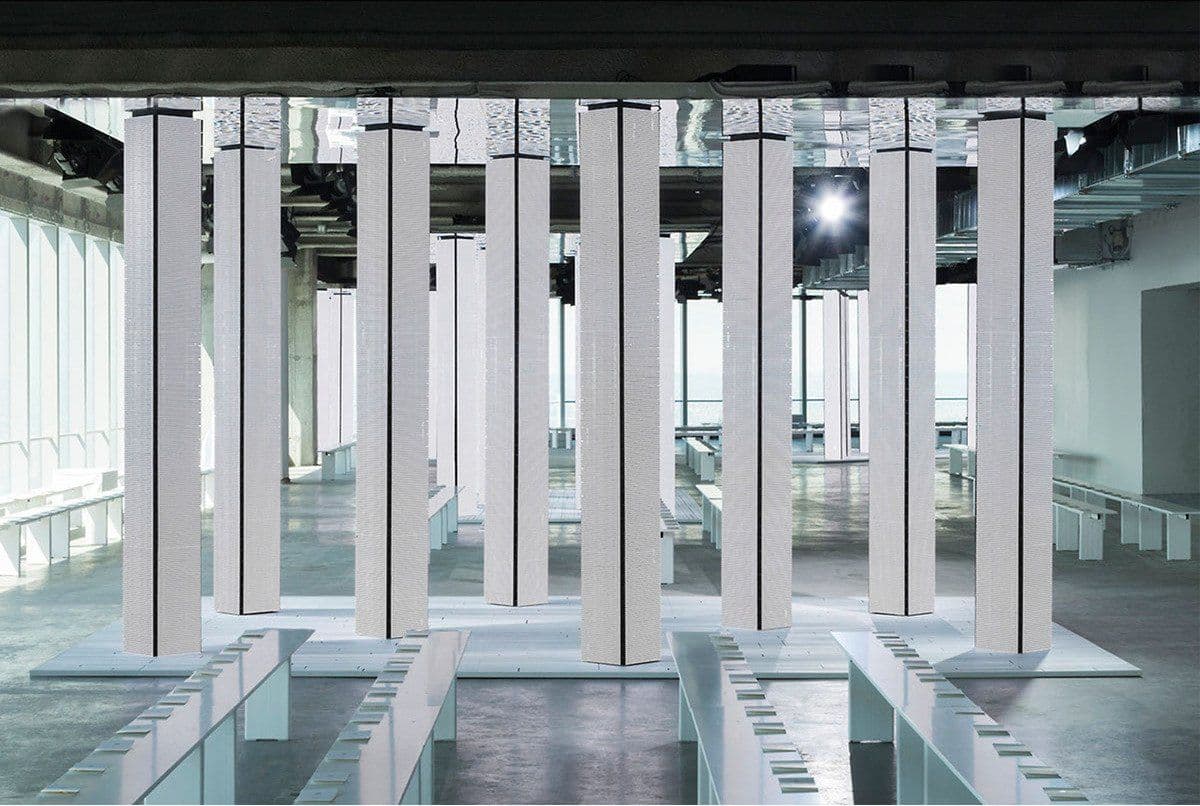 Runway space with the LED columns switched to a blank white pattern, empty benches lined up beneath an exposed concrete ceiling.