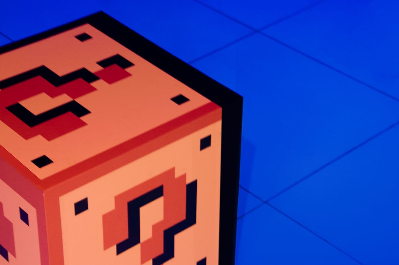Close-up of an orange pixel-art question-mark block sculpture against a blue backdrop.