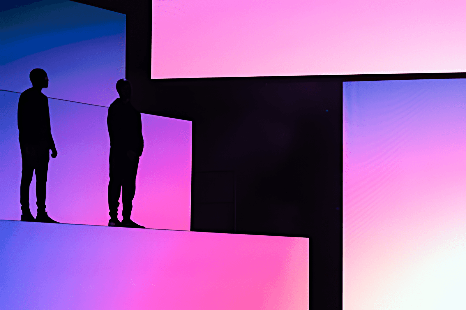 Two silhouetted figures standing on stage risers lit in a blue-to-pink gradient.